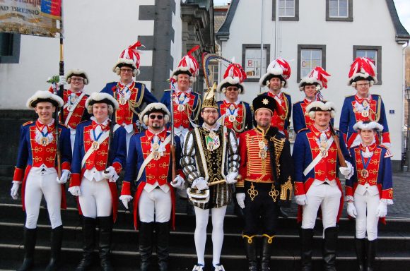 Personengruppe in festlicher Karnevalskleidung, auf einer Treppe vor historischen Gebäuden.