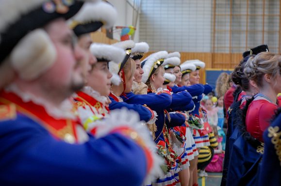 Gruppenschilde in traditionellen Kostümen mit feierlichen Gesten, farbenfroh und prächtig.